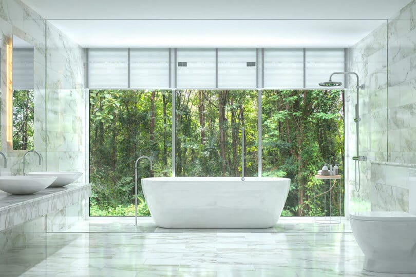 A freestanding bathtub in a room with floor to ceiling window behind it