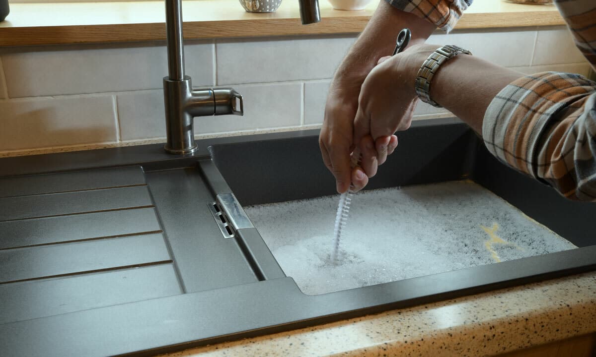 A person clearing a clogged sink drain with a plumber snake