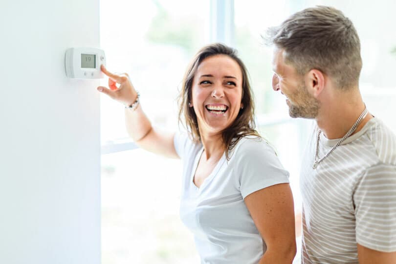 A happy couple pushing a button on a thermostat